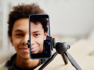 Half face portrait of smiling black teenager filming video for social ,media, focus on smartphone screen, copy space